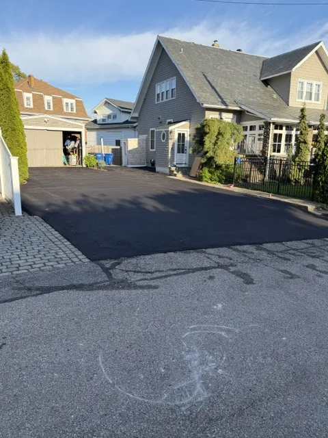 Fresh asphalt driveway at a shingled two-family home beside a detached garage